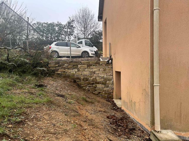 Murets en pierre repris le long de la maison, en soutènement du talus.
